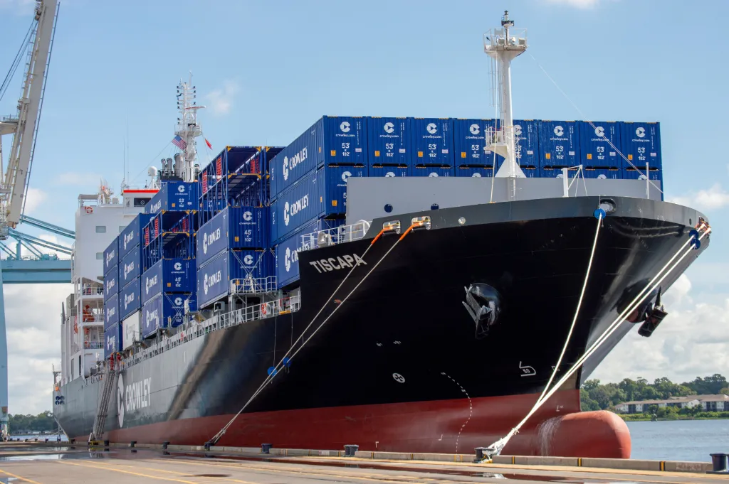 A container ship at port, with containers stacked on the dock.