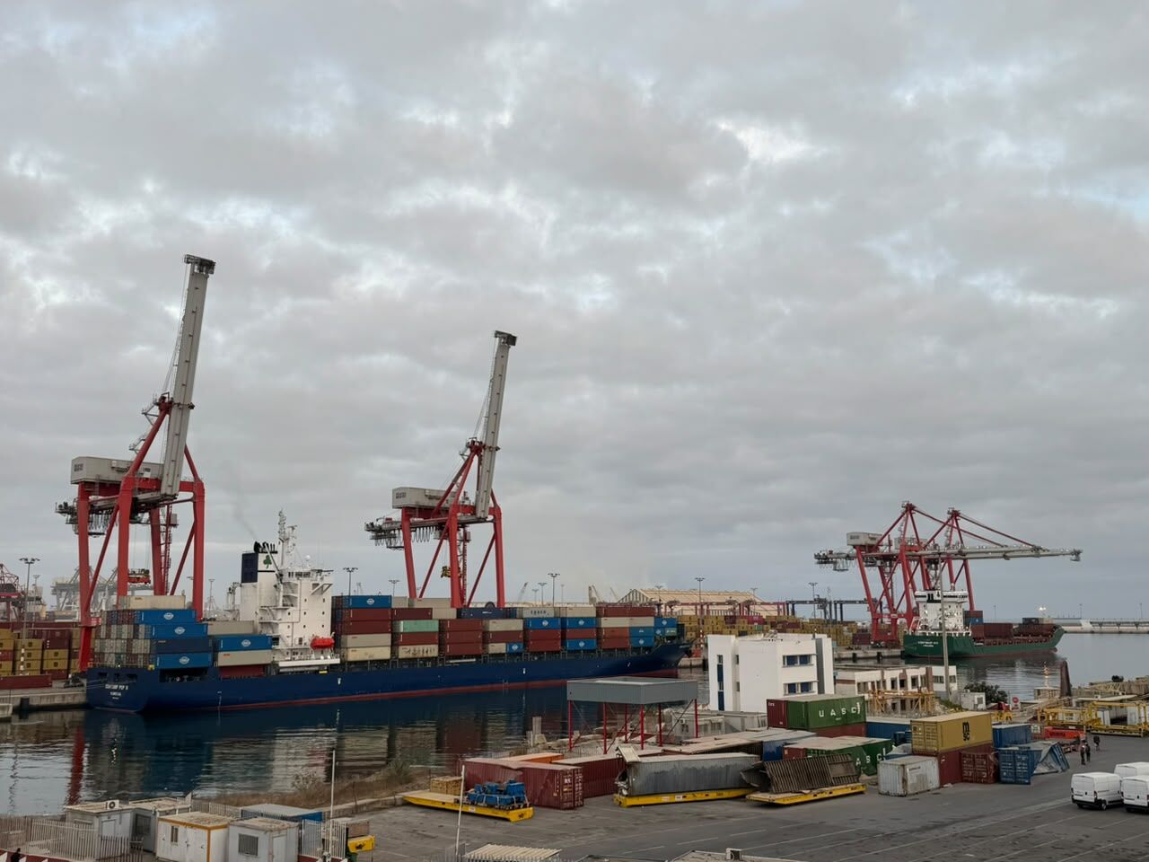 A large container ship being loaded or unloaded at a busy port terminal.