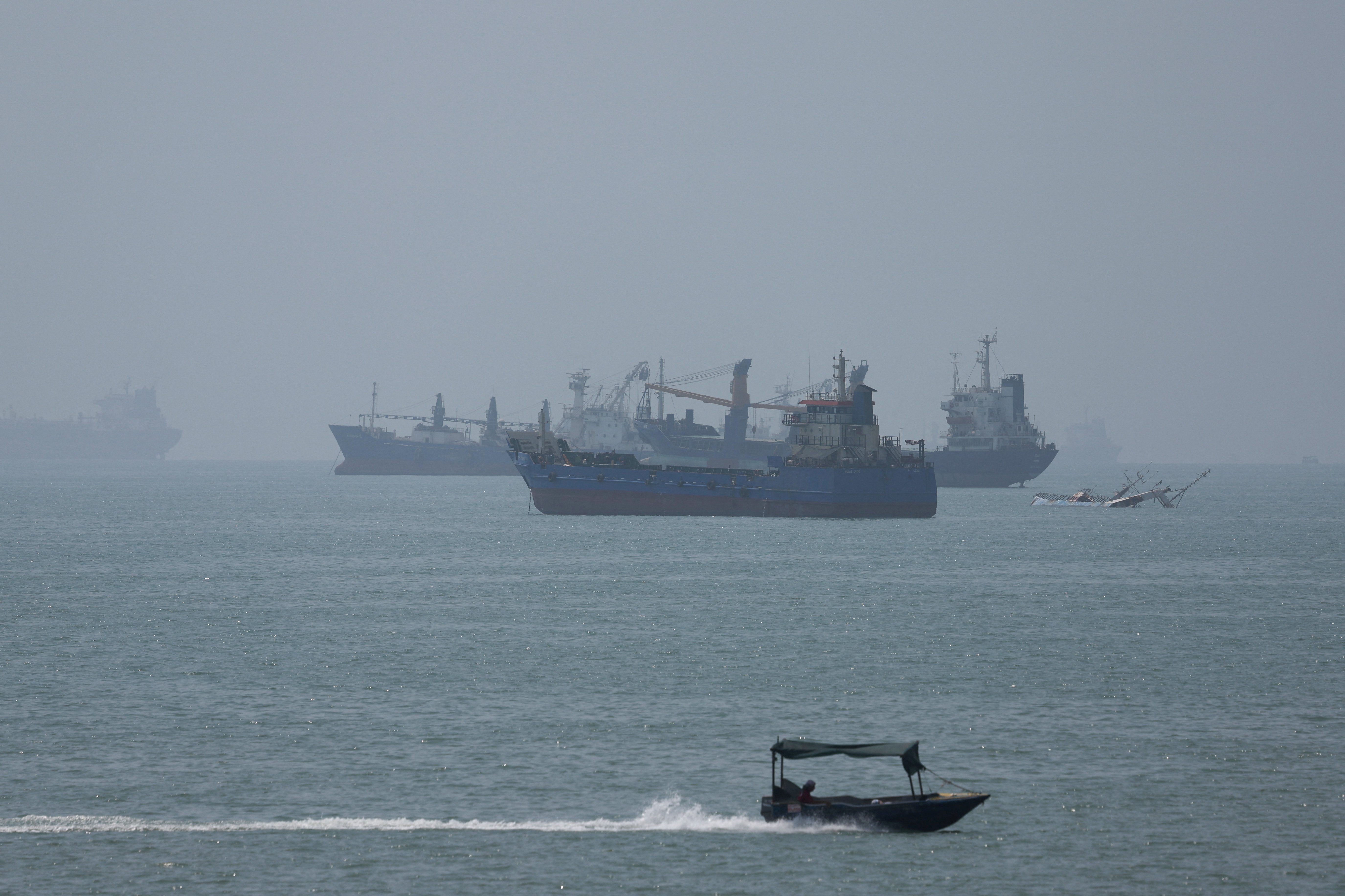 A large cargo ship navigating through a narrow strait, possibly the Strait of Hormuz, with land visible on both sides.