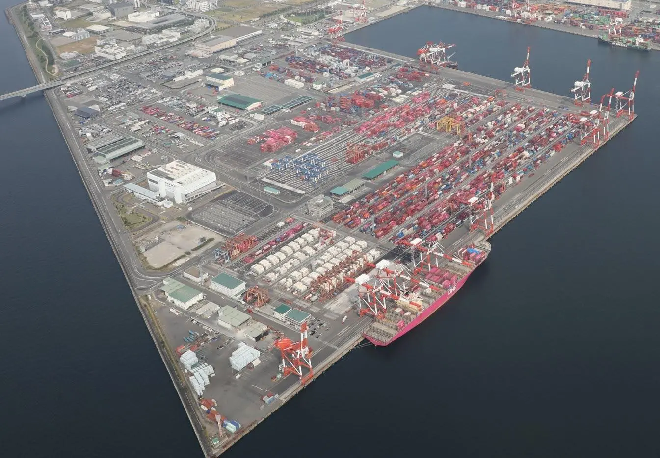 Container ships docked at a busy port terminal with cranes loading and unloading containers.