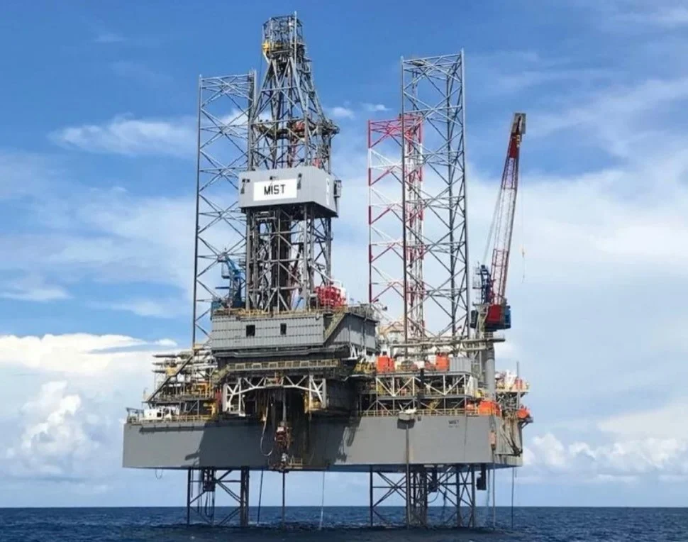 An offshore oil rig operating in the ocean, with a clear sky above.