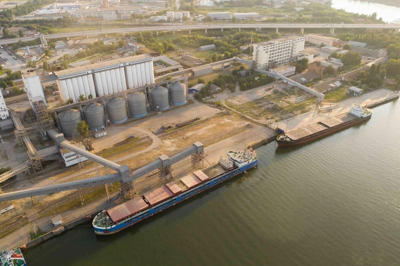 A large cargo ship being loaded with grain at a port terminal.